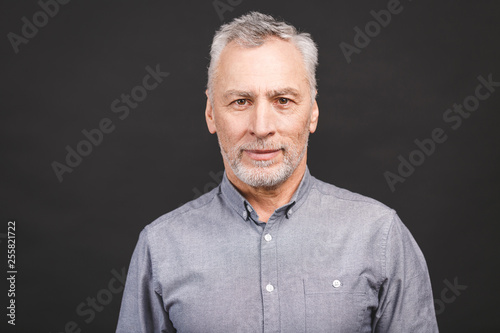 Portrait of a mature serious businessman isolated against black background. Happy senior man looking at camera with copy space. Close up face of happy successful business man.