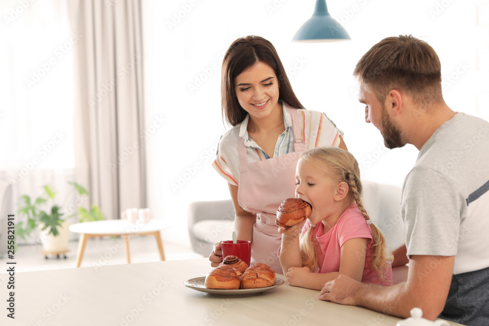 Happy couple treating their daughter with freshly oven baked bun in kitchen