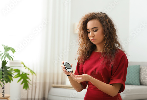 Young African-American woman using digital glucometer at home. Diabetes control photo