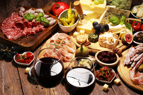 Italian antipasti wine snacks set. Cheese variety, Mediterranean olives, crudo, Prosciutto di Parma, salami and wine in glasses over grunge background.