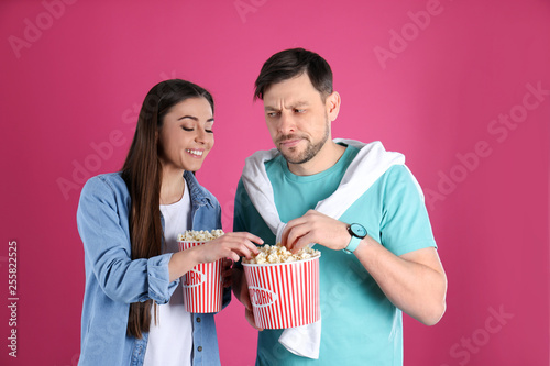 Young woman stealing popcorn from boyfriend on color background