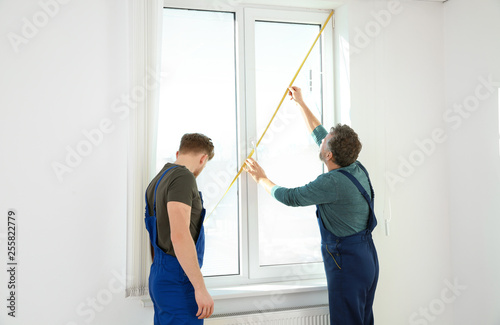 Service men measuring window for installation indoors