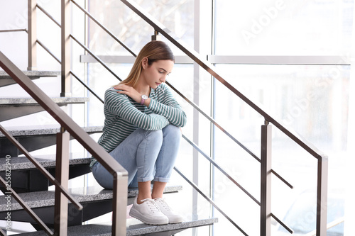 Emotional teenage girl sitting on stairs indoors