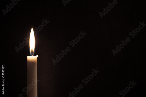White burning candle on a black background. Mourning, burning candle.