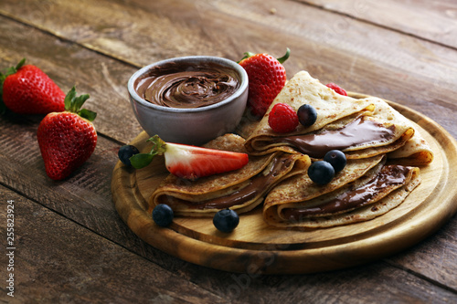 Delicious Tasty Homemade crepes with chocolate or pancakes with raspberries and blueberries on rustic wood photo