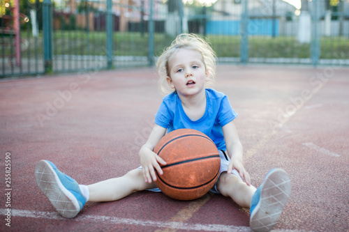 Little girl having a rest while sitting on basketball court