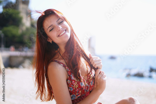 Happy Beautiful red hair Woman with cute smile in Red Dress on the Beach