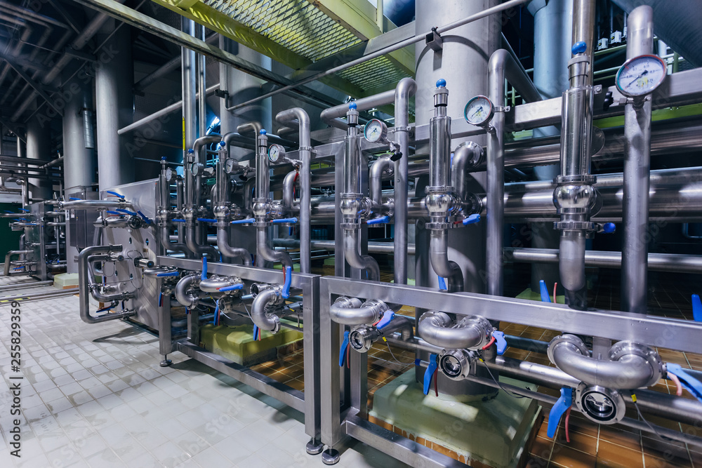 Modern brewery interior. Industrial stainless steel pipes connected with vats and control valves 