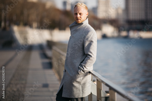 Blond in gray coat in city on walk near bridge next to river