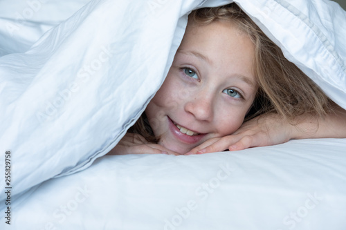 Tableau sur toile female child under duvet on bed looking out from underneath