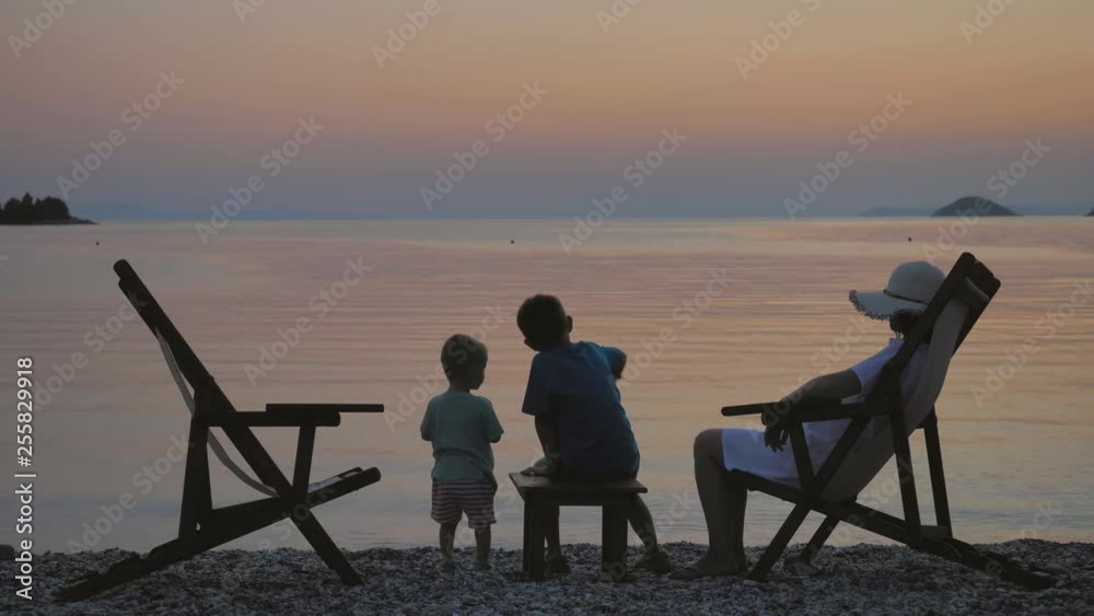Mother sit on chair on beach and children with back play, sunrise sky Mother sit on chair on beach and children with back play, sunrise sky