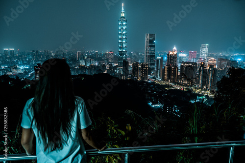 A woman overlooks the skyline of Taipei at night. Taiwan. 