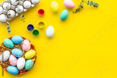 Colorful Easter eggs and paint for celebration on yellow background top view mock up