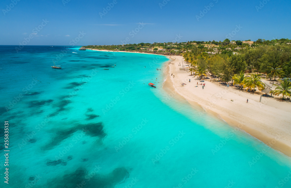 Aerial view of boats on tropical sea coast with sandy beach at sunny day. Summer holiday on Indian Ocean, Zanzibar, Africa. Landscape with boat, palm trees, transparent blue water, hotels. Top view