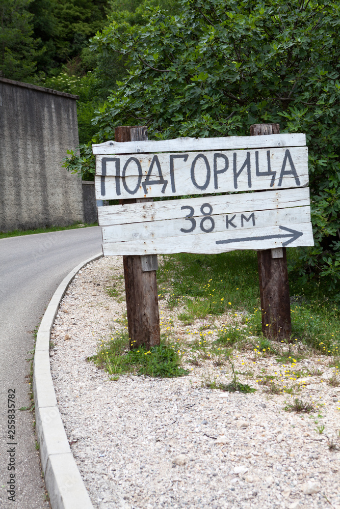 Wooden signpost with direction and distance to Podgorica city in countryside on rural asphalt road. Montenegro. Podgorica inscription in Montenegrin