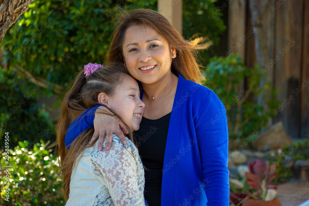 Latina Mother and Daughter smiling and laughing outside under a tree