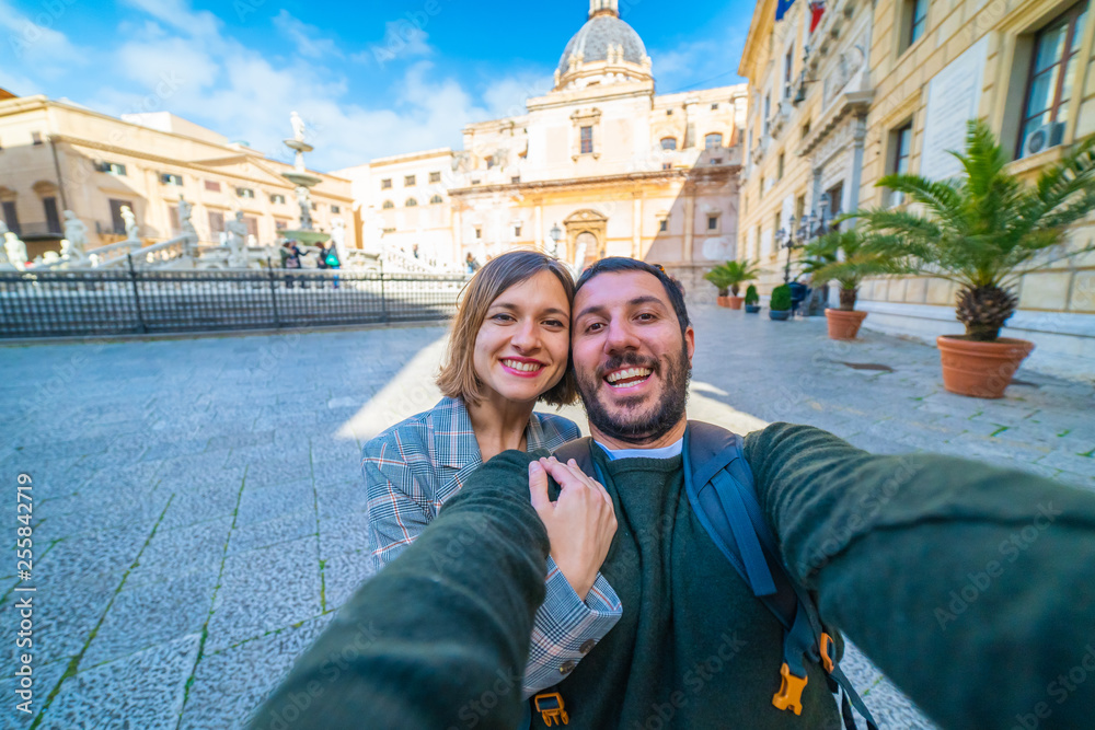 happy tourist couple traveling in Palermo, Sicily and taking selfie in Famous fountain of shame on baroque Piazza Pretoria, Palermo, Sicily, Italy. Italian holidays road trip