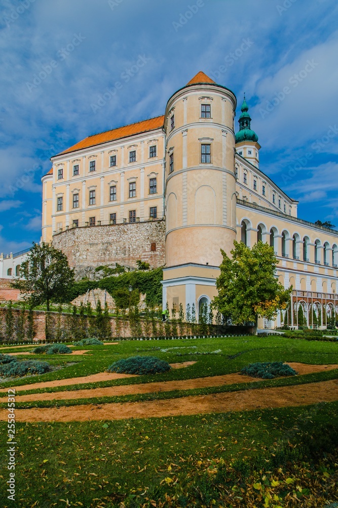Mikulov, Czech Republic / South Moravia - October 15 2016: Mikulov castle with yellow and white facade standing on a rock, green vegetation in a garden, sandy foot path, vertical image, sunny day