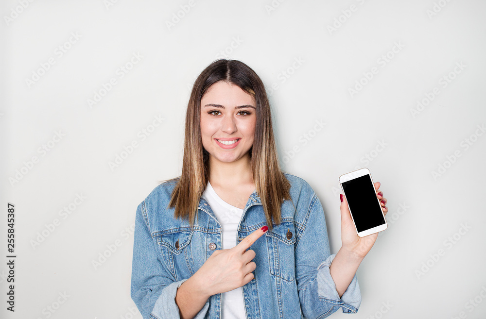 Smiling woman is pointing on smartphone standing on white background. Smiling woman is pointing on smartphone standing on white background.