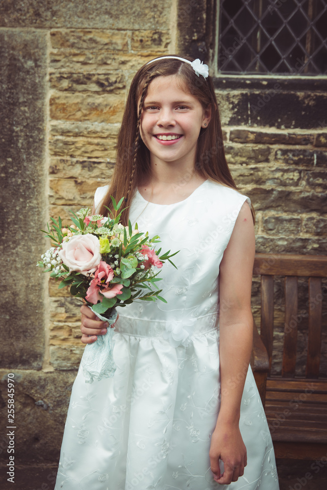 Beautiful smiling tween or teen young bridesmaid holding a rustic  wildflower bouquet, wearing a white dress, in front of a vintage stone  church Stock-foto | Adobe Stock