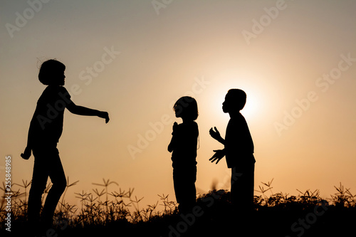 Silhouette group children playing on meadow at sunset time.