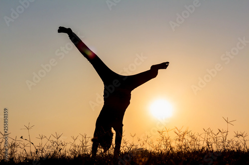 Happy child playing upside down outdoors in summer park walking on hands at sunset.silhouette