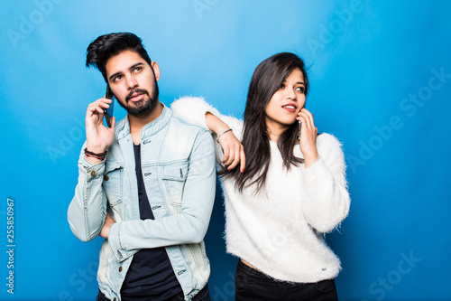 Young indian couple talking on their phones standing isolated on blue background