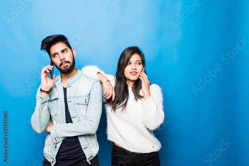 Young indian couple, man and woman talking on the phone isolated on blue background