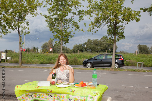 Roadside picnic. A lonely middle-aged woman drinks wine at a table by the side of the road.Concept introvert's birthday, introverted person. © ozerkina