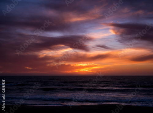 Vivid  dramatic sky over sea at sunset with blue orange gradient and dark clouds