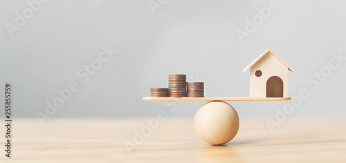Wooden home and money coins stack on wood scale. Property investment and house mortgage financial real estate concept photo