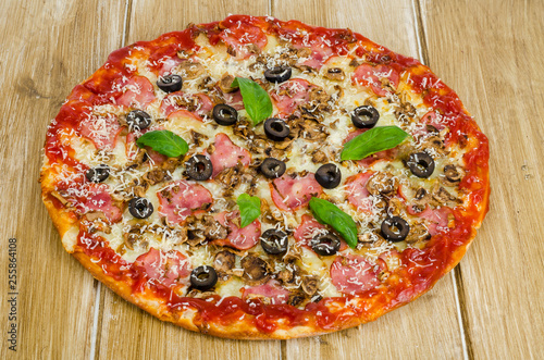 Pizza with ham, mushrooms and olives on wooden surface.