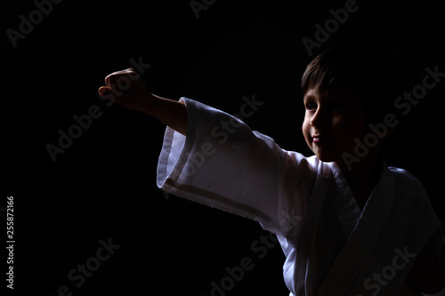 Karate boy in white kimono posing on dark background. Child ready for martial arts fight. Kid fighting at Aikido training. Best for martial fights and sports concept.