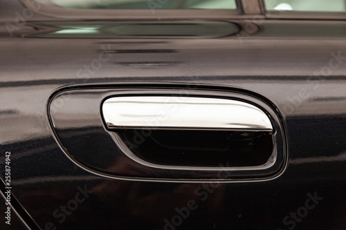 View on closed black front door with handle made from chromium of luxury car after detailing and polishing © Aleksandr Kondratov