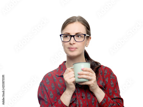 A portrait of pretty smiling young brunette woman with delicate makeup sitting on white background. She holding a cup with tea or coffee in right hand. Horizontal studio image with high resolution.