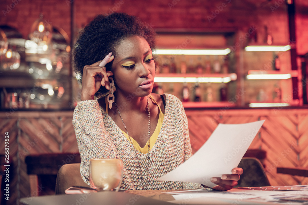 Serious Afro-American woman concernedly looking at papers in hands Serious Afro-American woman concernedly looking at papers in hands