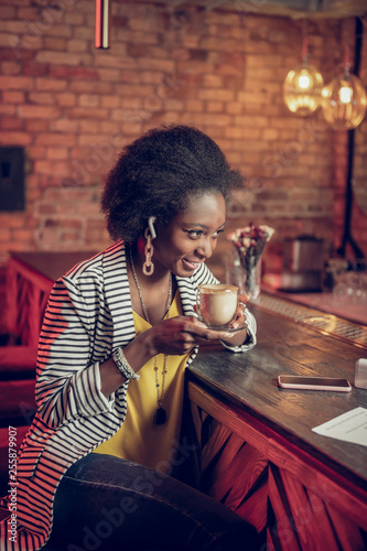 Charming African-American lady having coffee sitting at bar counter