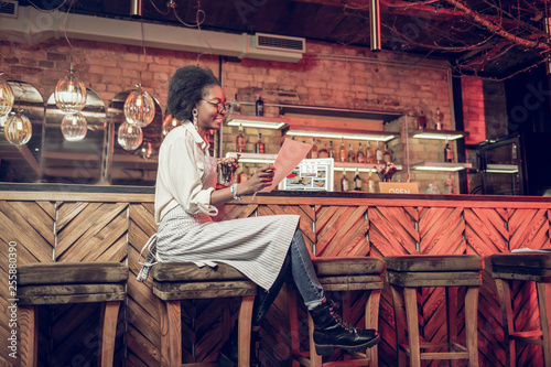 Bewitching barmaid thoroughly reading menu while sitting at bar chair