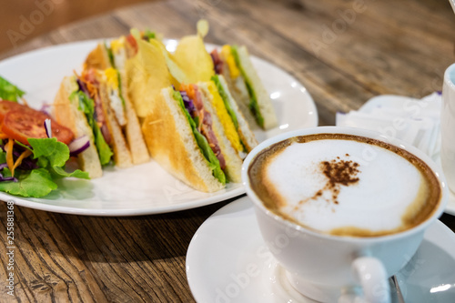 A cup of hot milk coffee with milk and homemade sandwich (Latte coffee or Cappuccino coffee) on the wooden table in coffee shop.