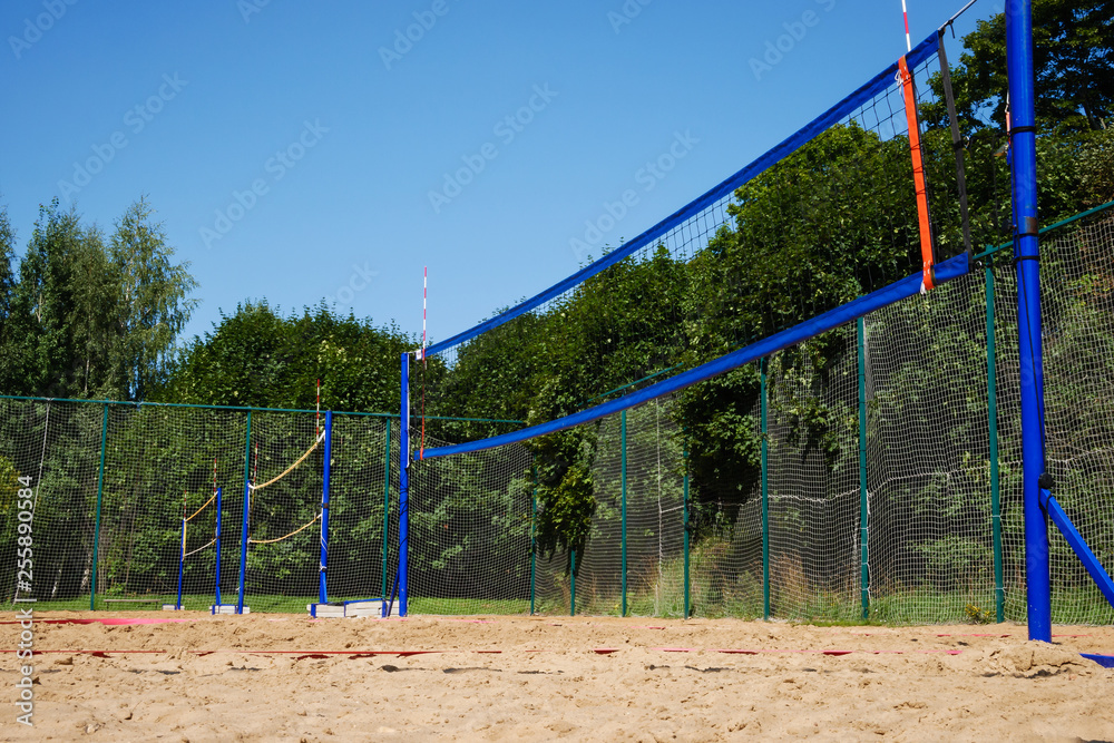 Low angle view on rows of volleyball nets on blue poles on empty sand court surrounded by lush green trees on summer day