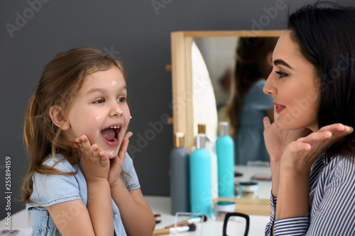 Young mother and emotional little girl with cream on her face