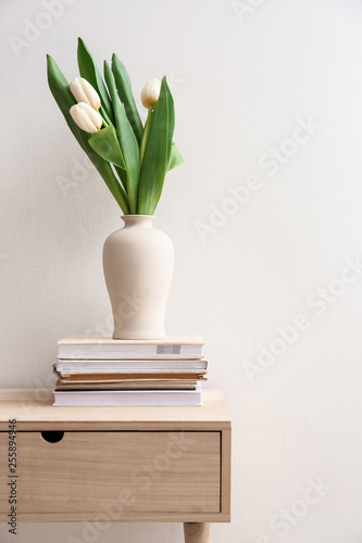 Vase with bouquet of flowers and books on table against light background
