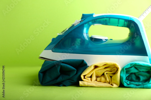 Iron with clean clothes on color background