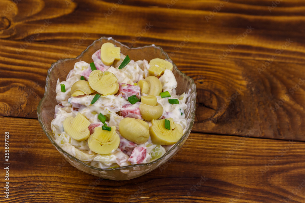 Potato salad with marinated mushrooms, sausage, onion and mayonnaise on wooden table