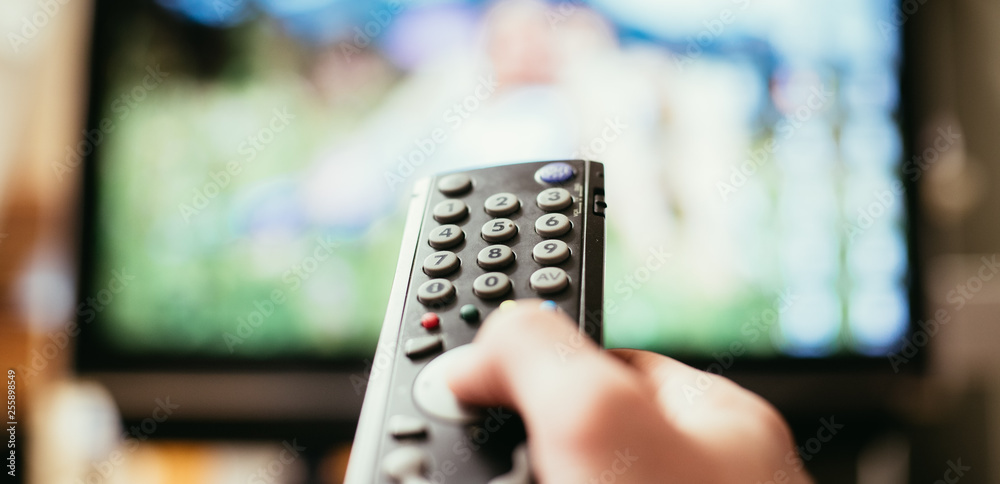 Male hand is holding TV remote control, streaming on a smart TV. Male hand is holding TV remote control, streaming on a smart TV.