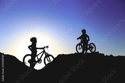 Silhouette of two little girls with bicycles at sunset