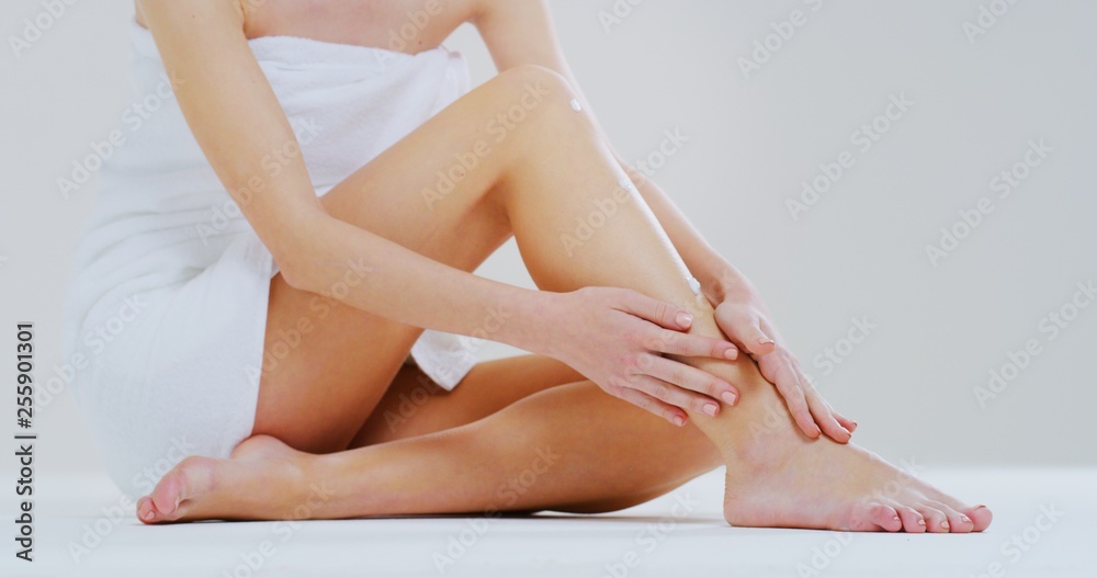 Obraz premium Close up of young beautiful woman with perfect body touching gently her hairless soft and silky legs after depilation isolated on a white background.