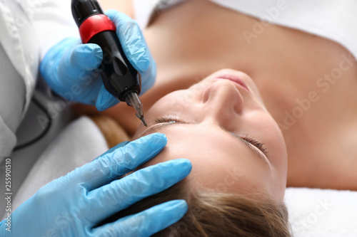 Young woman undergoing procedure of permanent makeup in beauty salon