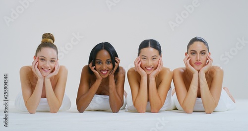 Portrait of beautiful young women of different ethnicities with perfect face lying on the floor and smiling in camera isolated on a white background.