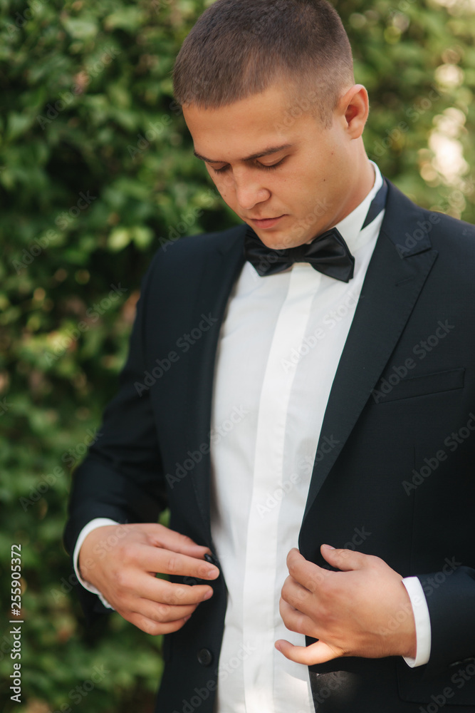 Young man walking in the park. Handsome groom in black suit Young man walking in the park. Handsome groom in black suit